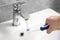 Man holding electric toothbrush under flowing water above sink in bathroom, closeup