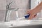 Man holding electric toothbrush under flowing water above sink in bathroom, closeup