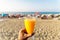 A man holding a fresh glass of orange juice with a straw in front of the beach