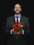 Man holding fresh red tulip bouquet in his hands. Model is bald with grey beard, wearing classic grey suit. Handsome male with