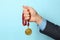 Man holding golden medal on color background, closeup.