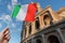 Man is holding italian flag in hand. Colosseum in background. Travel in italy concept.