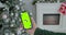 Man holding a mock-up smartphone greenscreen chrome key in New Year decorated room. Closeup of male hands holding black