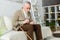 Man holding pill and glass of water while sitting on sofa near walking cane