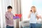 Man holding plastic basin under water leakage from ceiling while woman calling plumber