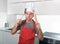 Man holding skimmer and rolling pin in apron and cook hat at home kitchen