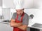 Man holding skimmer and rolling pin in apron and cook hat at home kitchen