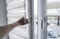 Man holding window handle on a plastic window with white fabric roller blinds in the living room. Close up on roll