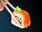 Man holding wooden chopsticks sushin, on top of wasabi sushi. dark background