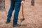 A man holds an ax in his hand lowered down in the autumn forest close up