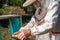 A man holds a frame with bees in his hands. A suit for a beekeeper, a jumpsuit and a mesh cap protection on the head.