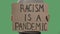 A man holds in front of him a poster from a cardboard box with the words RACISM IS A PANDEMIC. Isolated a green screen