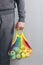 A man holds in his hands a reusable cotton shopping string bag, a multicolored rainbow with green apples inside. gray background.