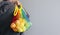 A man holds in his hands a reusable cotton shopping string bag, a multicolored rainbow with green apples inside. gray background.