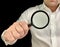 A man holds a magnifying glass in front of him. A man in a white shirt shows a magnifier, on a black background. Concept: