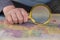 A man holds a magnifying glass in his hand over a map. A middle-aged man with a magnifying glass in a gold frame. The names are