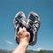 Man Holds Old Running Sneakers In Hand On Background Of Bue Sky And Mountains