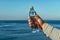 A man holds a plastic bottle of drinking water in his hand, standing on the ocean