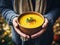 A man holds a plate of pumpkin soup against the background of autumn leaves. Generated by AI