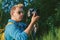 A man holds a professional photo-video camera in his hands. Against the backdrop of green nature and forest