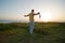 Man holds a protective face mask in his hand stands on shore of the ocean at sunrise.