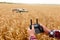 Man holds remote controller with his hands while copter is flying on background. Drone hovers behind the pilot in wheat