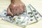 a man holds a stack of hundred-dollar bills lying on the table with his fist