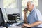 Man in home office on telephone using computer