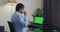 Man at home sitting on a couch working on green mock-up screen laptop computer.