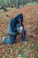 A man in a hood, bowing his head, stands on one knee in prayer and holds a cross below