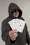 A man in a hood holds playing cards in his hands