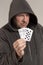 A man in a hood holds playing cards in his hands