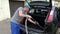 Man hoovering black car boot with vacuum cleaner outdoor. 4K