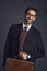 The man of the hour. Studio portrait of a stylishly dressed young man carrying a bag against a gray background.