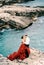 Man hugs a woman in a red dress while standing on the stones above the sea