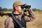 Man hunter with shotgun looking through binoculars in forest