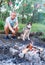 Man with husky dog preparing campfire in summer forest. Hipster treveler outdoors in the wood
