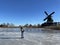 Man ice skating on a frozen lake with the windmill from IJlst in the background