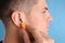 Man inserting foam ear plug on light blue background, closeup