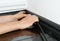 A man is installing a black plastic skirting board to hide cables and wires. A homeowner is concealing wiring in the trunking of a