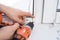 Man installing gray pleated blinds on the window with screwdriver