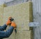 A man installs a layer of thermal insulation on the wall of the stairs outside - using mineral wool panels.