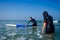 Man instructor demonstrating how to paddle in the water by hands on surfboard to indian woman in surf class in Goa sea
