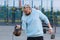 A man with an interesting braid hairstyle in a blue hoodie works out early in the morning on the street and lifts a kettlebell