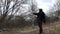 A man in a jacket with a hood on is walking in a spring park along the river. Breaks branches flowering vines. Spring landscape.