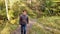 Man in jeans walks on path in park on sunny day. Autumn forest road landscape.