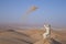 Man in kandura in a desert, throwing sand