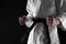 Man in keikogi with black belt on dark background, closeup. Martial arts uniform