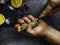 A man with a knife opens a fresh oyster. Dark stone background with lemon, ice, berries, selective focus