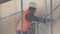 Man laborer in orange uniform vest scratches wall with hammer on scaffolding